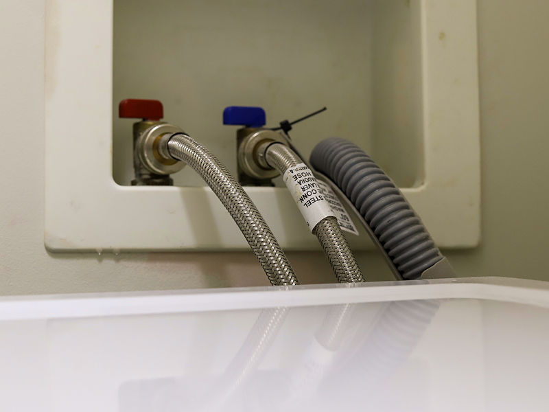Close-up image of a white sink with two hoses, indicating water flow or drainage connections.
