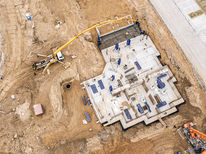 A construction site featuring a crane and a truck, with building materials and workers in the background.