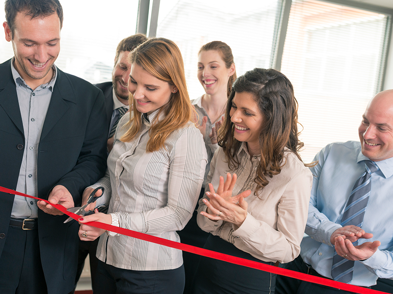 A group of individuals joyfully cutting a ceremonial ribbon at an event, symbolizing a grand opening or celebration.