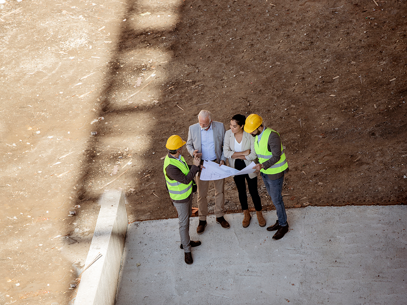 everal workers in hard hats and vests gathered at a construction site, reviewing blueprints and discussing the project.
