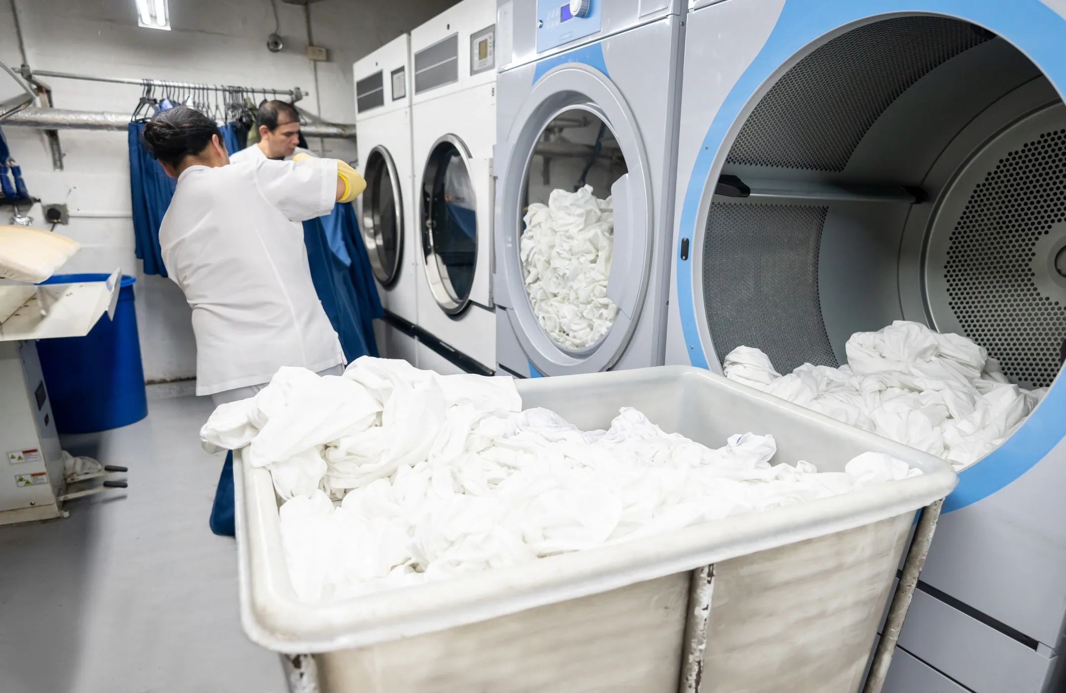 Industrial laundry with workers and large dryers.